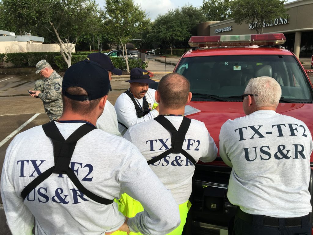 TX-TF2 plans members gathered around the hood of a vehicle discussing operations for the day